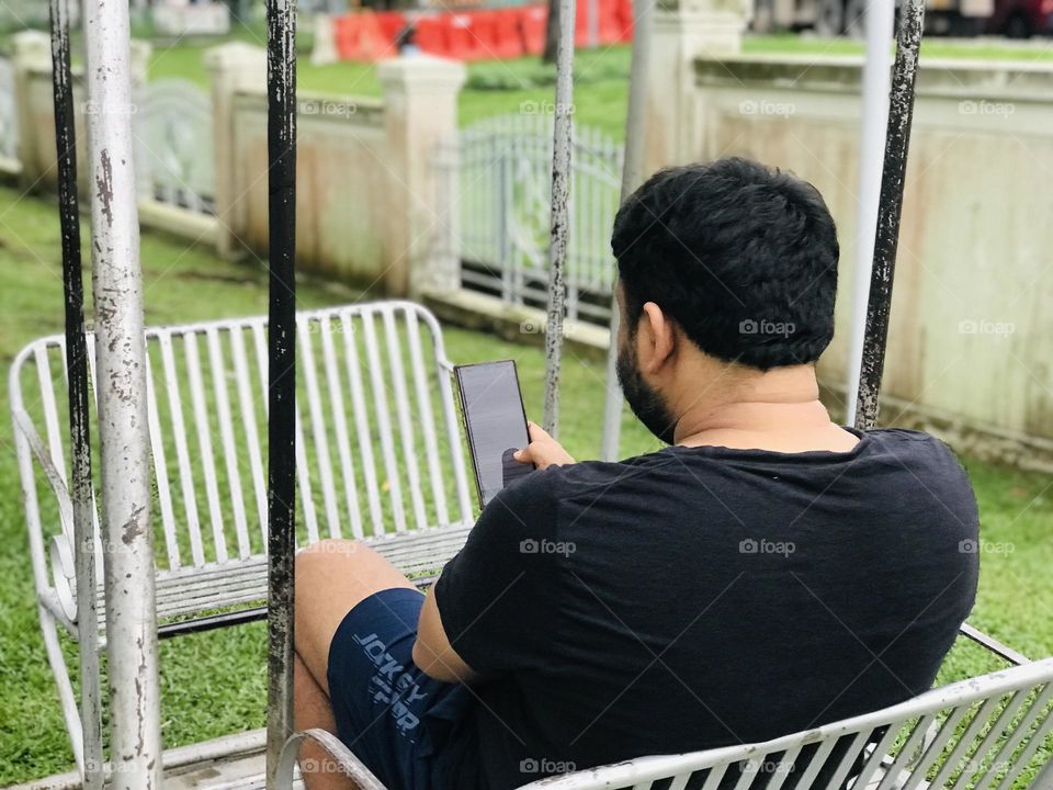 Person looking in phone while swinging on swing at outside.