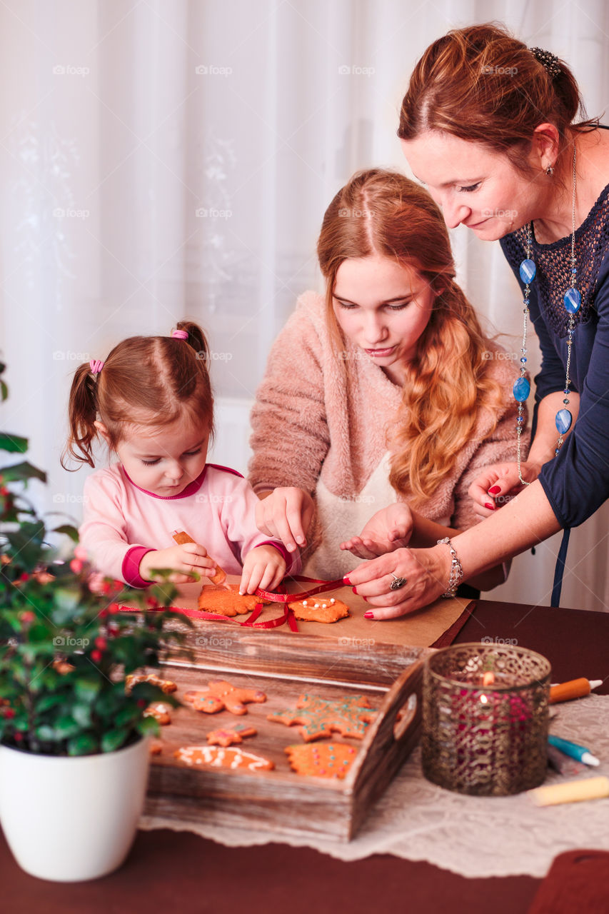 Family decorating baked Christmas gingerbread cookies with frosting