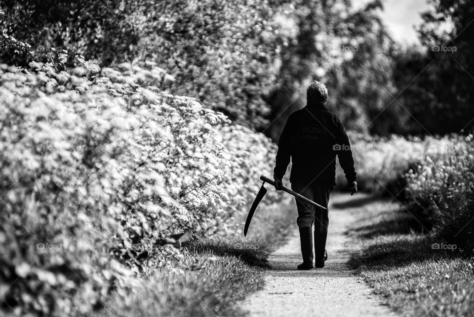 Man with a scythe walking down a path