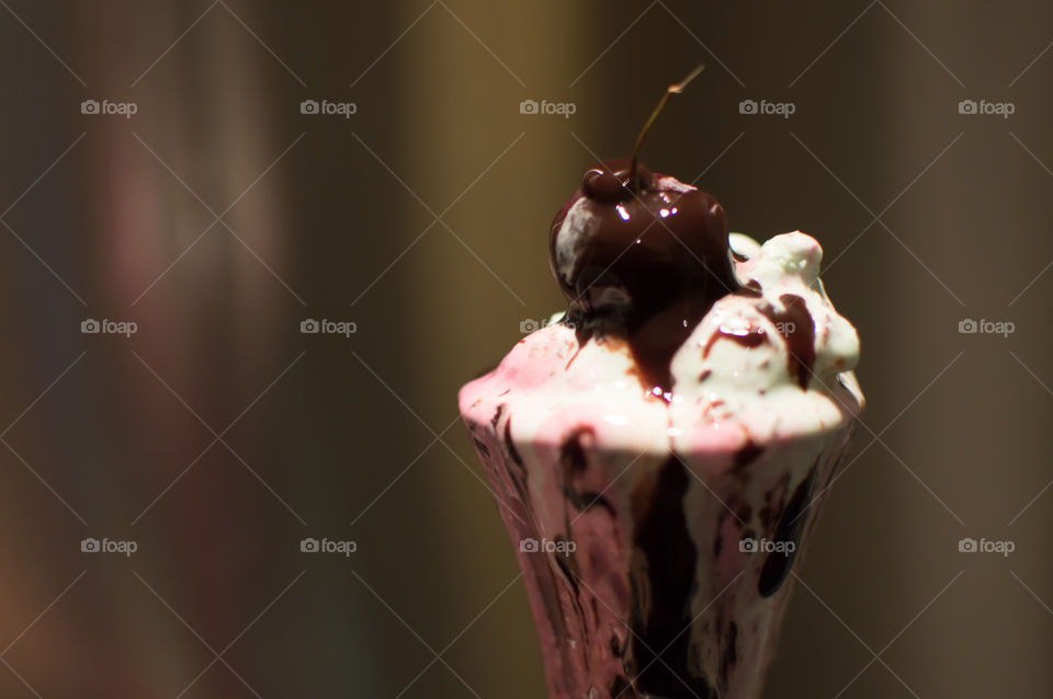Decadent hot fudge flowing over dark cherry on top of flowing melting pink and green ice cream in a delicious mess, gourmet indulgence food art photography 