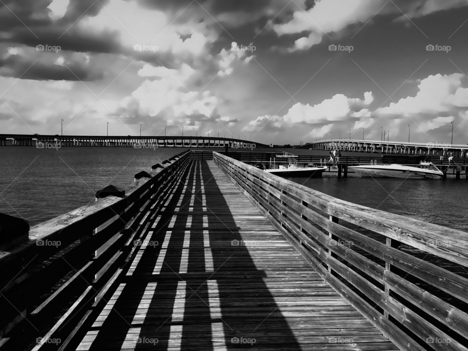 Long pier over the water on a sunny day casting light and shadow in symmetrical lines in monochrome.