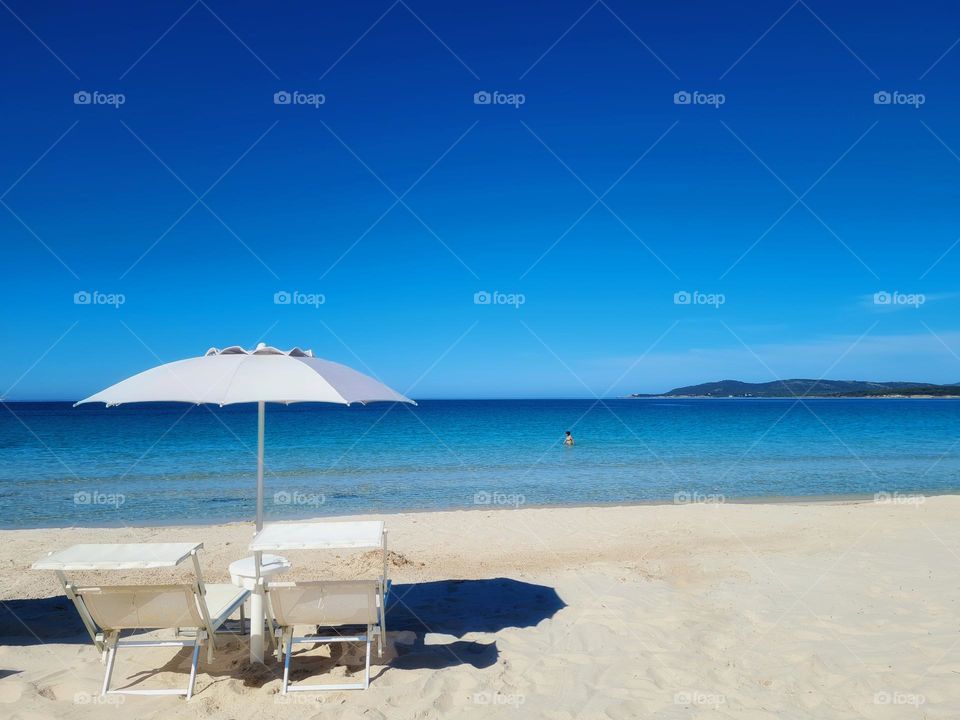 white beach umbrellas and deck chairs and in the background the crystalline sea of ​​Sardinia