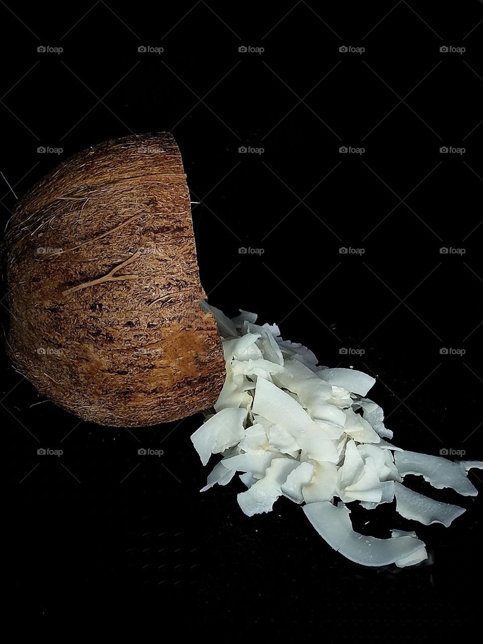 Half of a coconut with coconut flakes scooped out. Black background