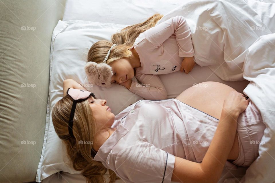 Pregnant mother and daughter sleeping in bed