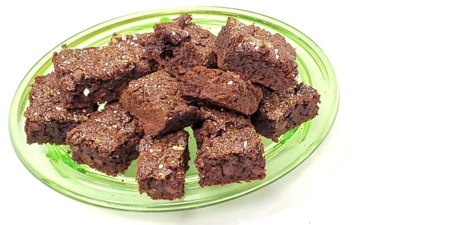 Chocolate brownies on a green glass plate with a white background 