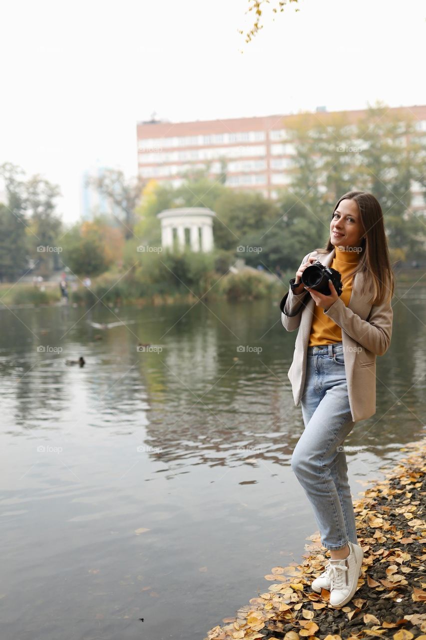 Girl photographer with a camera in her hands on the shore of the autumn lake
