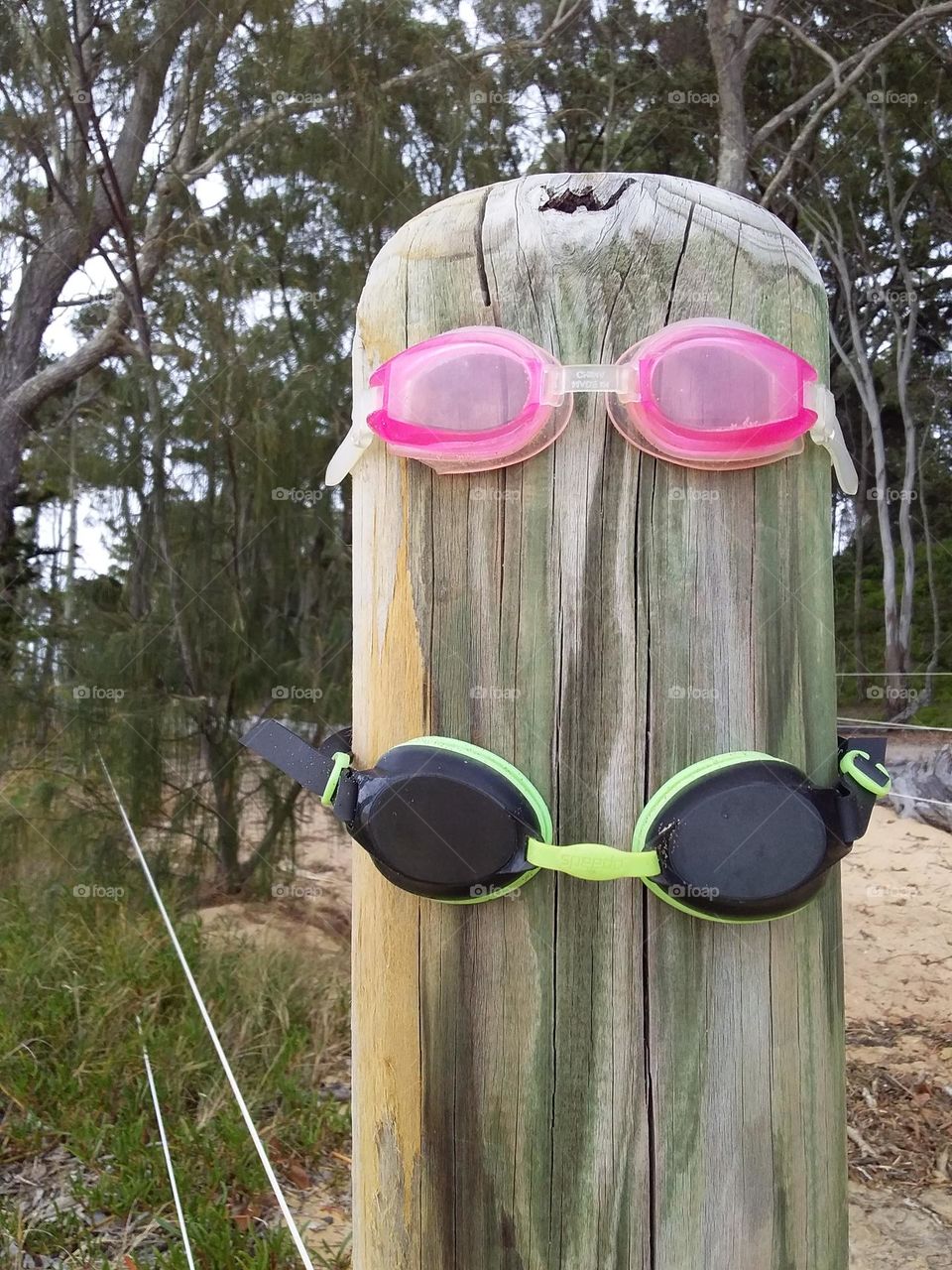 2 happy pairs of swimming goggles on a post at the beach
