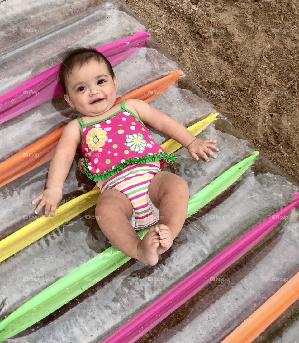Baby girl in swimsuit on a floatie at the beach