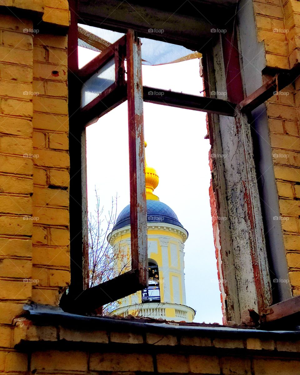Old brick wall with an old broken wooden frame from the window through which the church is visible