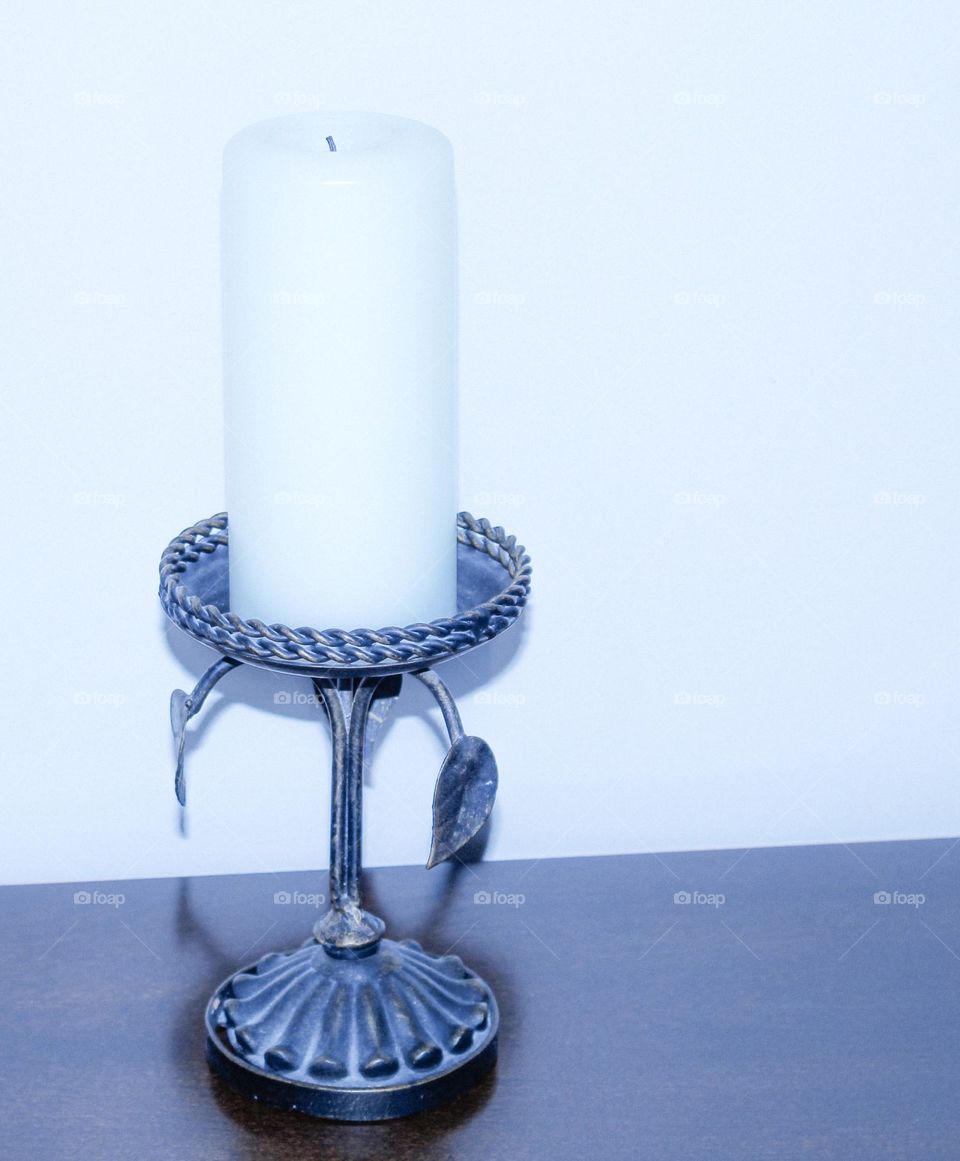 A white column candle in an old silver and blue rustic holder on a table against a white wall. 