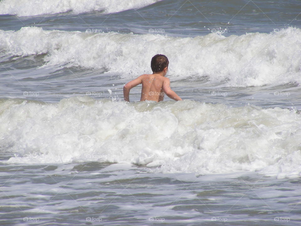 Boy standing in the ocean water as the waves come towards him