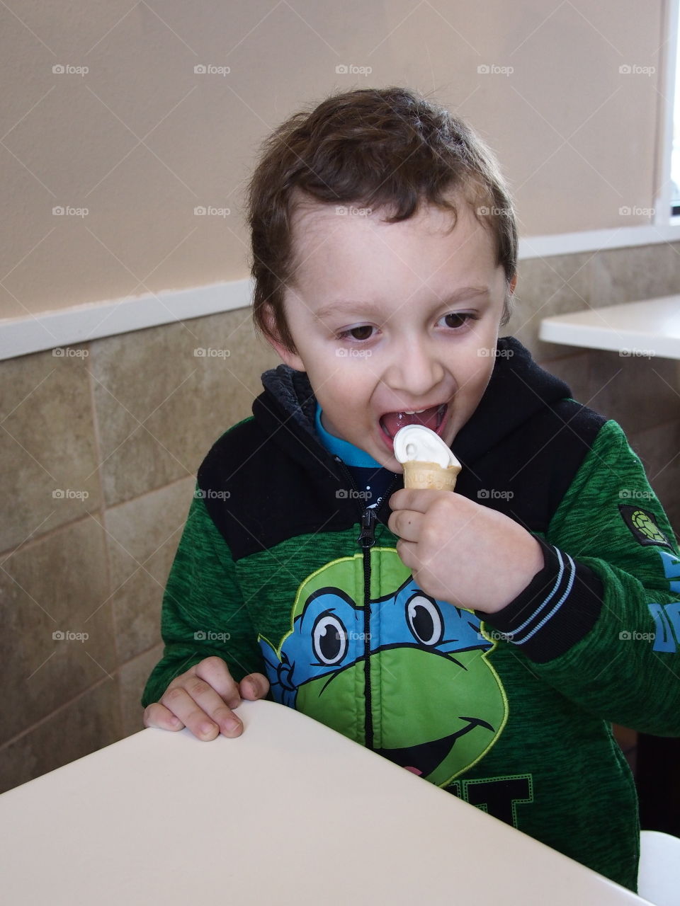 A little boy really enjoys his small vanilla cone that really hits the spot. 