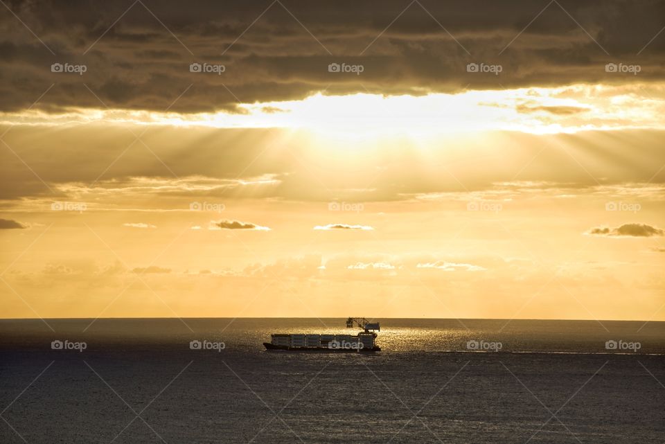 Container ship passing by a sunburst off Waikiki beach, Honolulu 