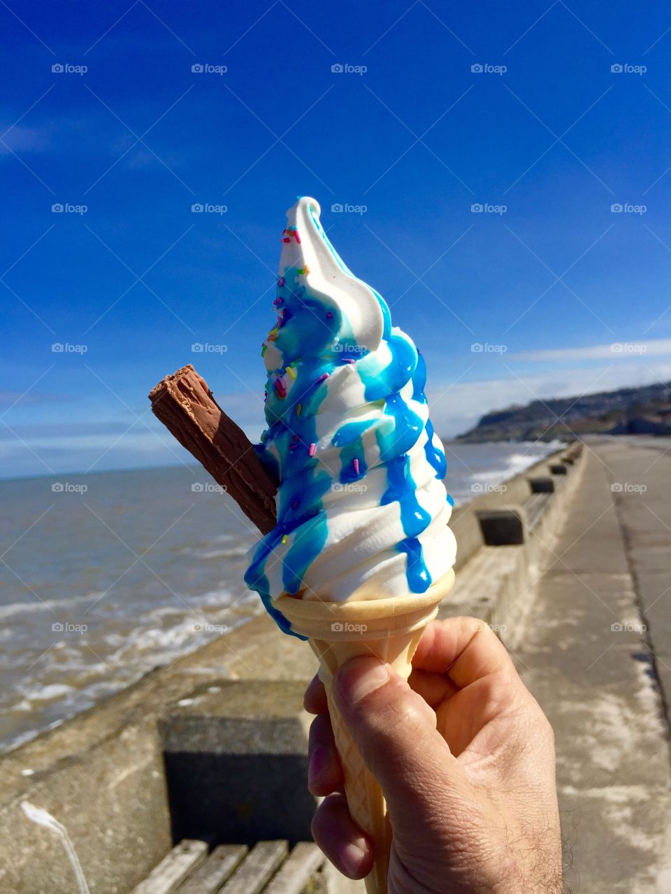 Person holding ice cream cone at beach side