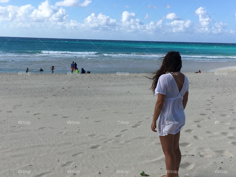 Girl in white dress gazing out to the sea on beautiful white beach with turquoise waters 