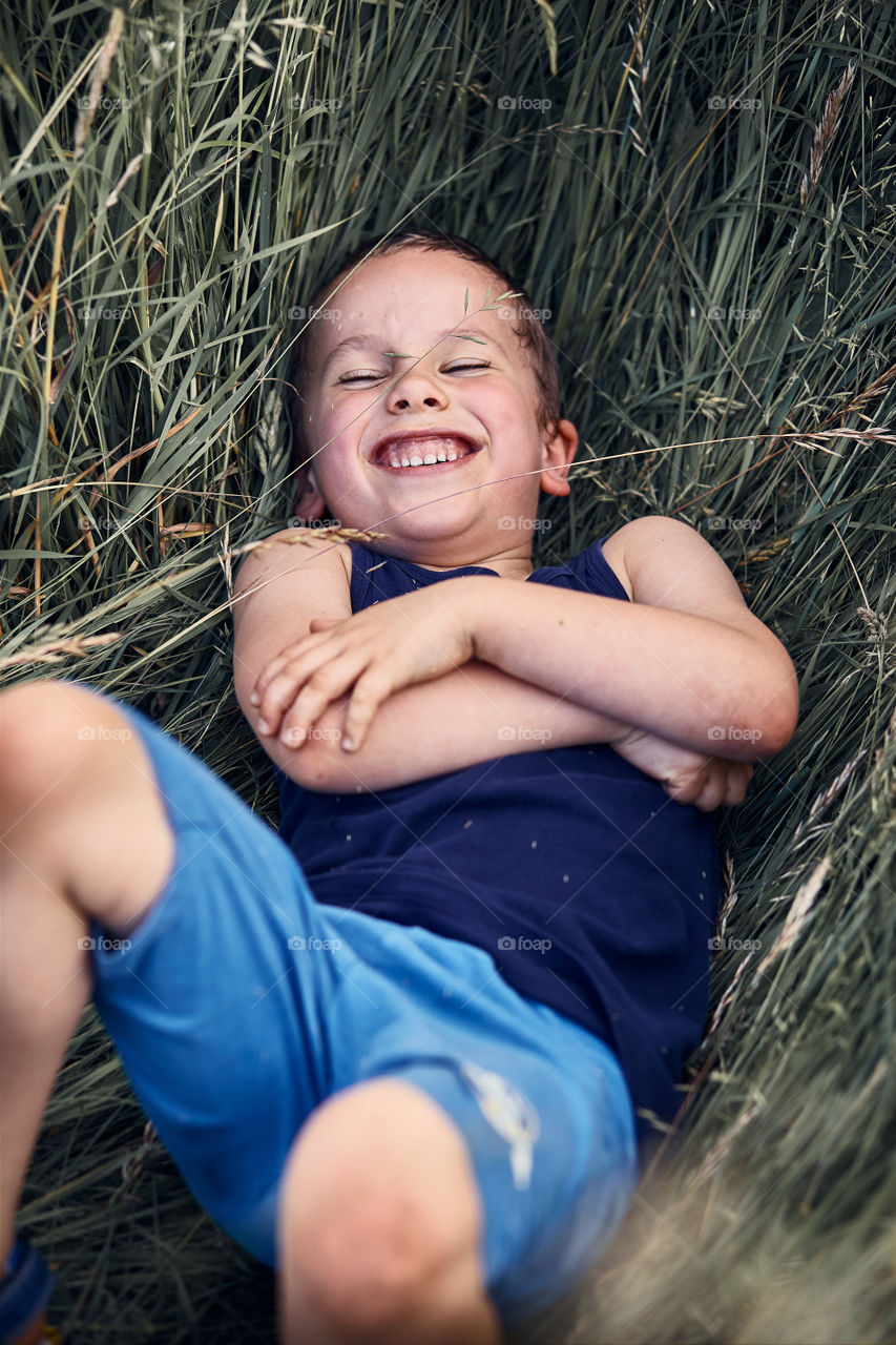 Little happy kid playing in a tall grass in the countryside. Candid people, real moments, authentic situations