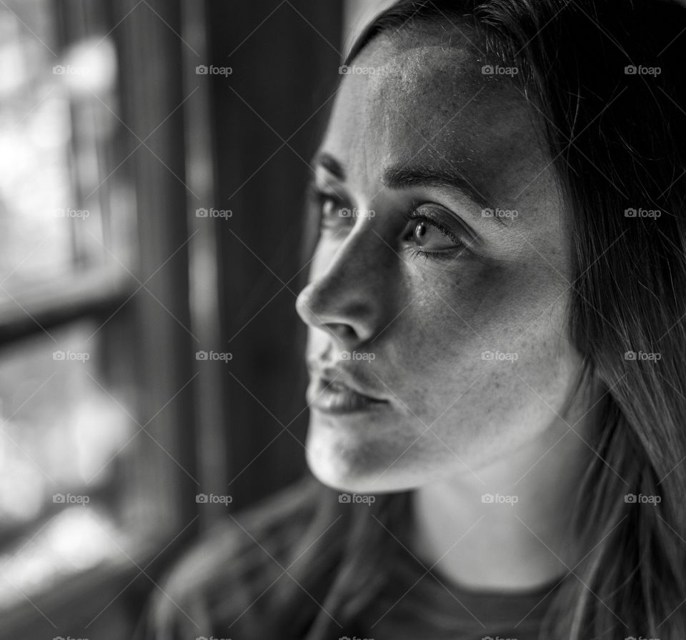 Image of a girl mysteriously looking through a window in black and white. 