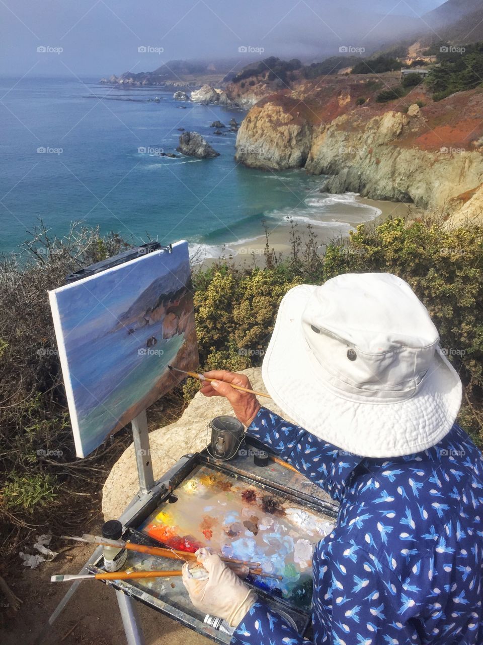 A painter tries to put on canvas the beauty of California coast. Then she can just take the painting home and remember the magic feeling you get when you sit on that coast and feel the ocean breeze on your face! 