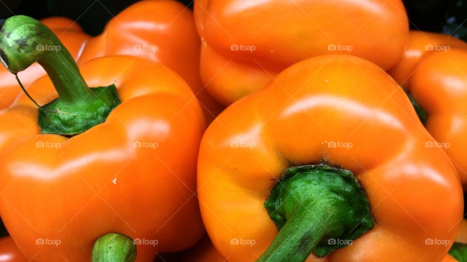 Heap of orange bell peppers with green stems