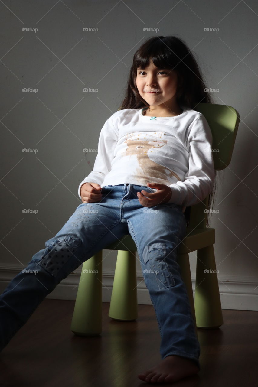 Cute little girl with long hair is sitting on a chair, portrait