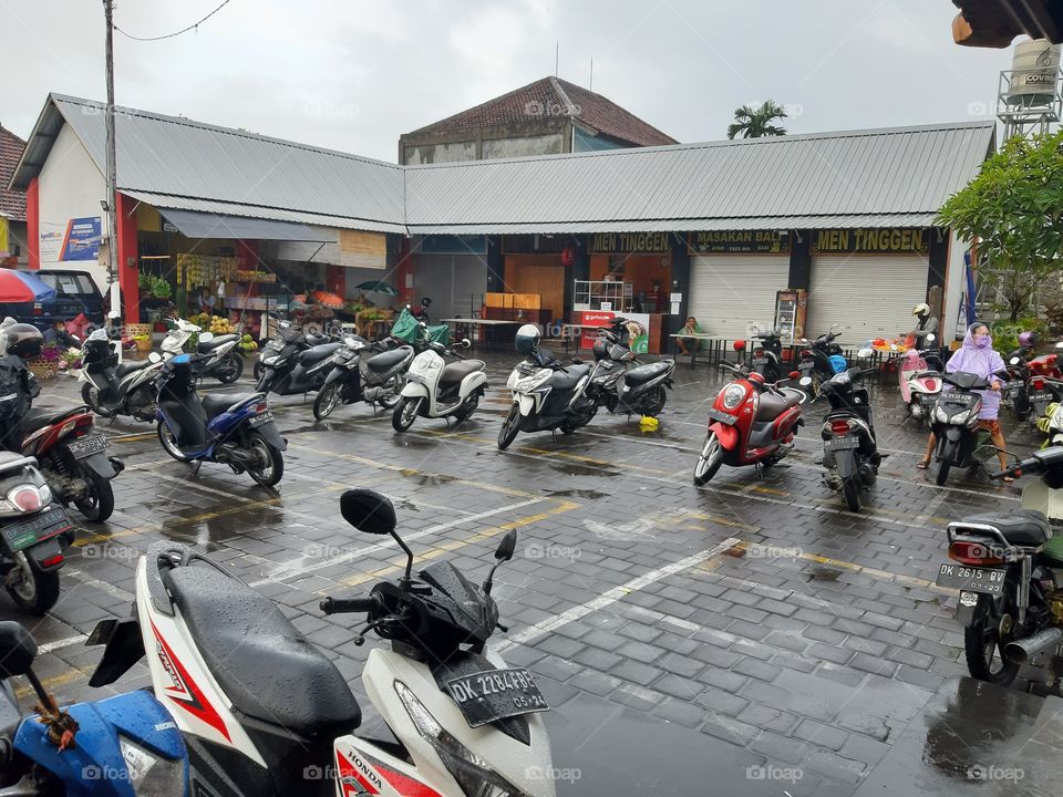 The situation of a traditional market in rainy day. There are some motorbike getting wet due to raining.