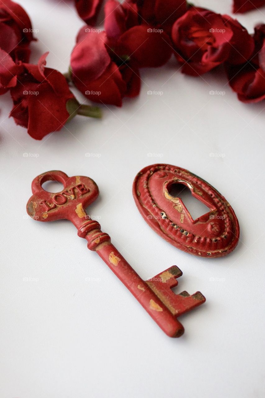 Red, metal, vintage key and keyhole with red, silk rose buds on white marble surface