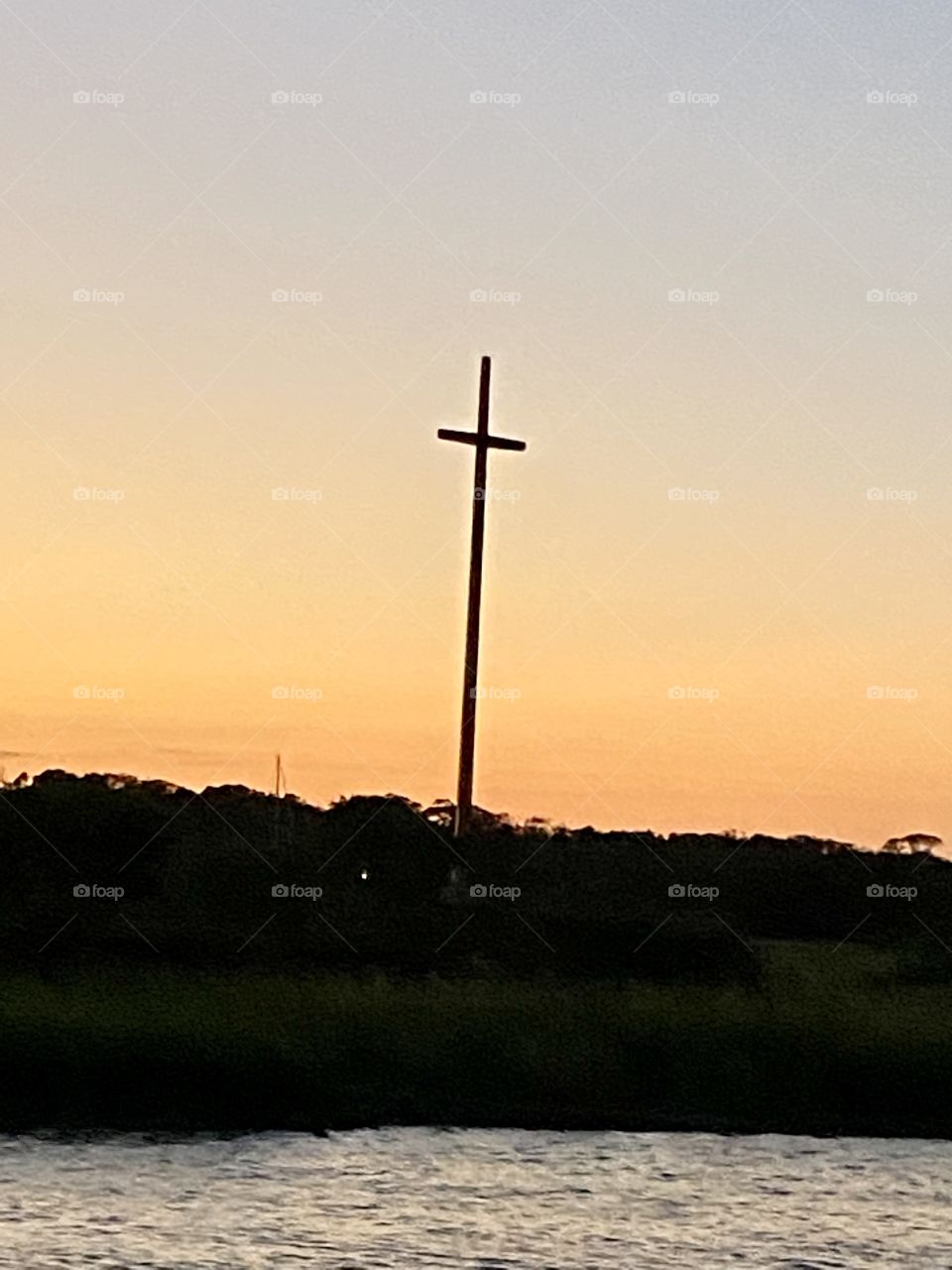 A very tall cross rising up above the land with an orange twilight sunset