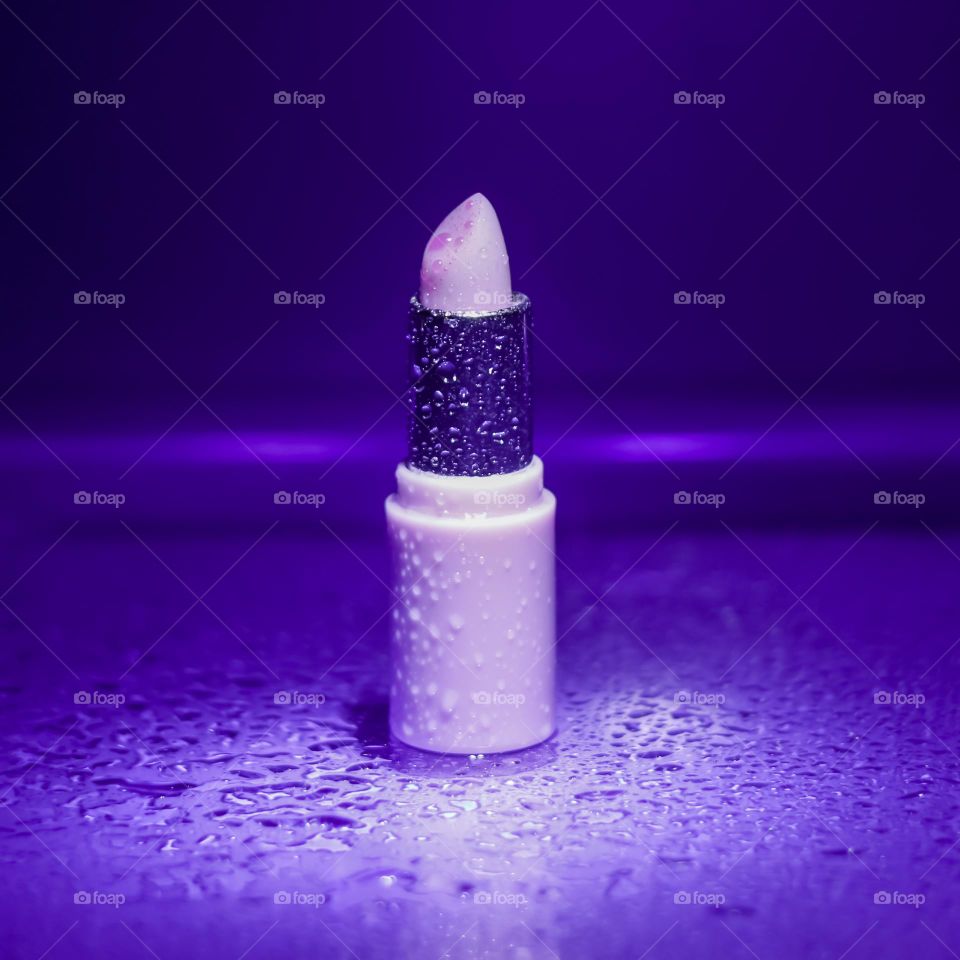 A lilac coloured lipstick sprayed with water under purple lights 