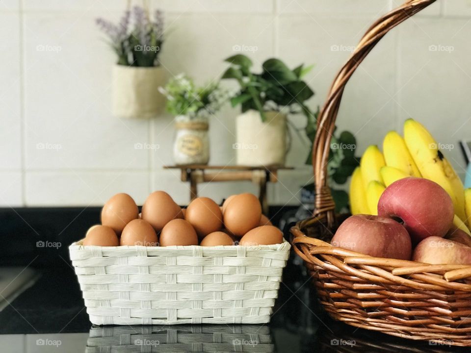 Eco friendly wooden bamboo baskets filled with nutritional fruits and eggs and background covered with wooden stand and eco friendly flower vases.