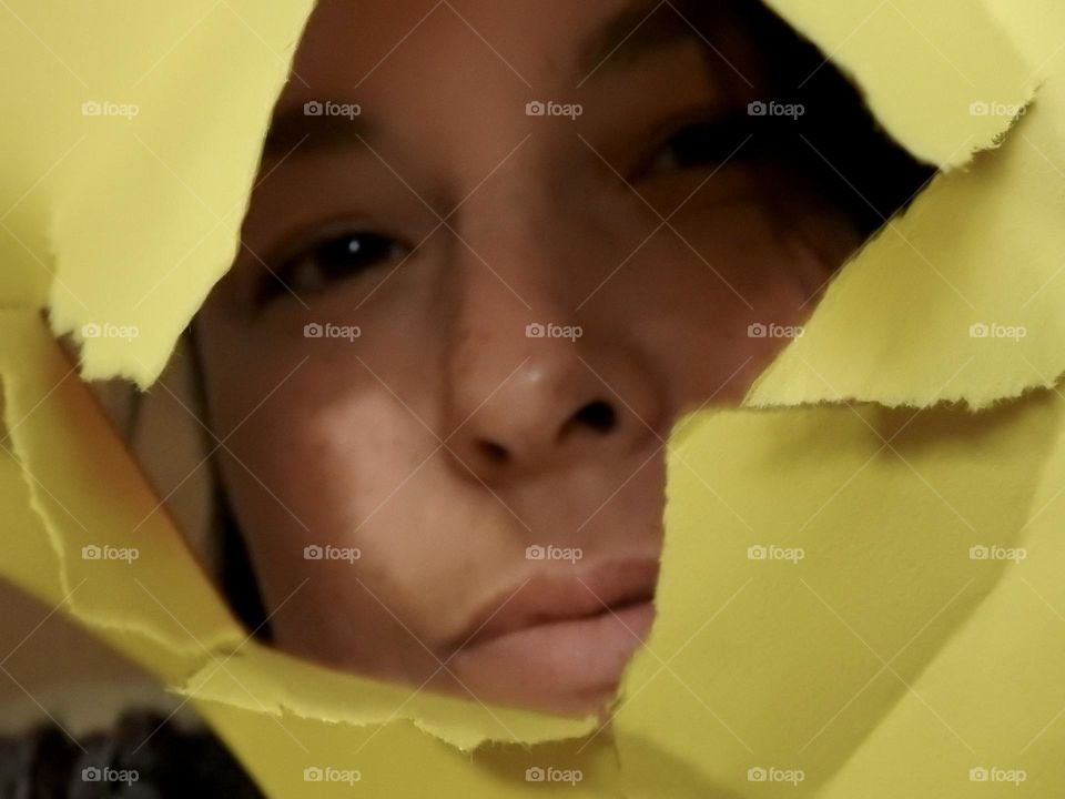 Face skin in the forties of a woman with freckles and brown hair seen through a broken yellow paper.