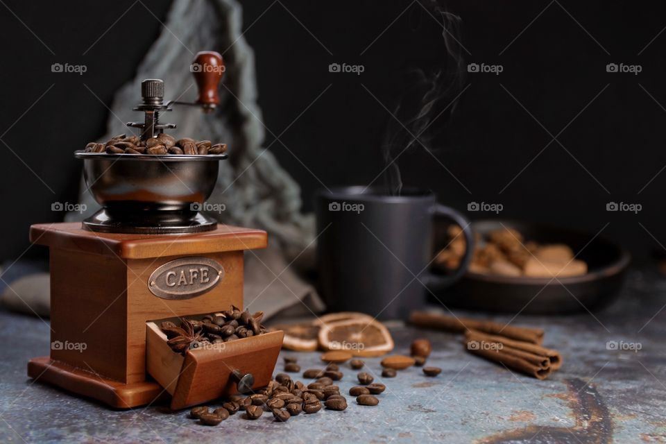 a cup of hot coffee and a wooden coffee grinder with coffee beans