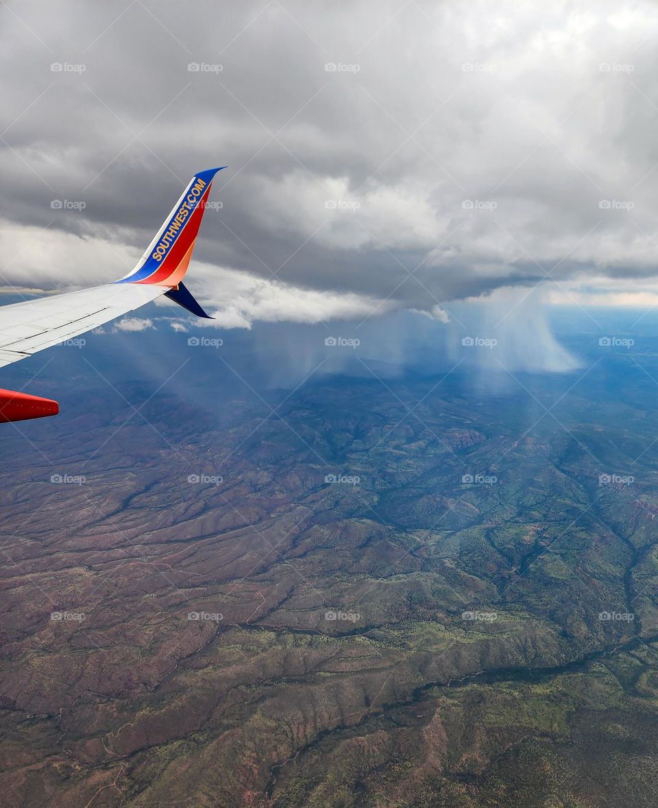 Huge rainshafts descend from dark clouds during an afternoon monsoon in Arizona while the plane descends into Phoenix Sky Harbor International Airport