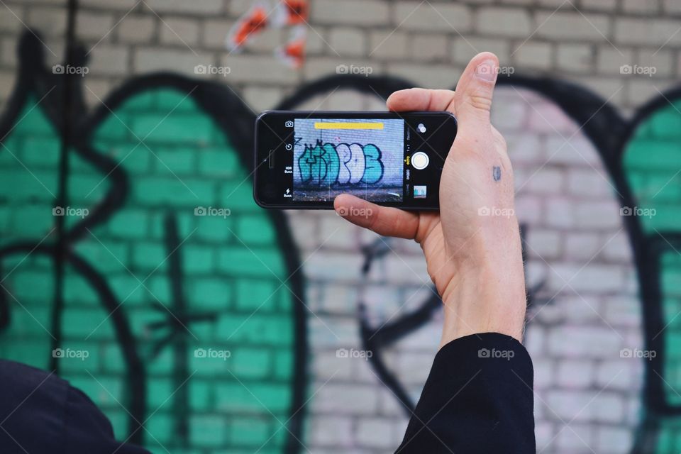 Hand of man taking photo of graffiti with smartphone