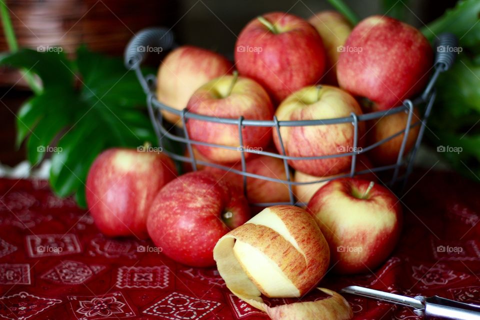 Fruits - Gala apples in a wire basket with a partially peeled apple and peeler on a red bandana-print tablecloth