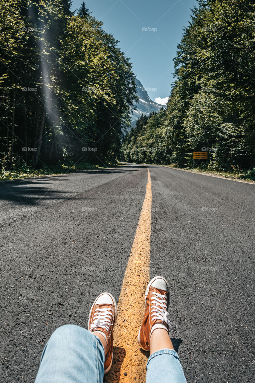 female legs on the road with yellow line and mountains