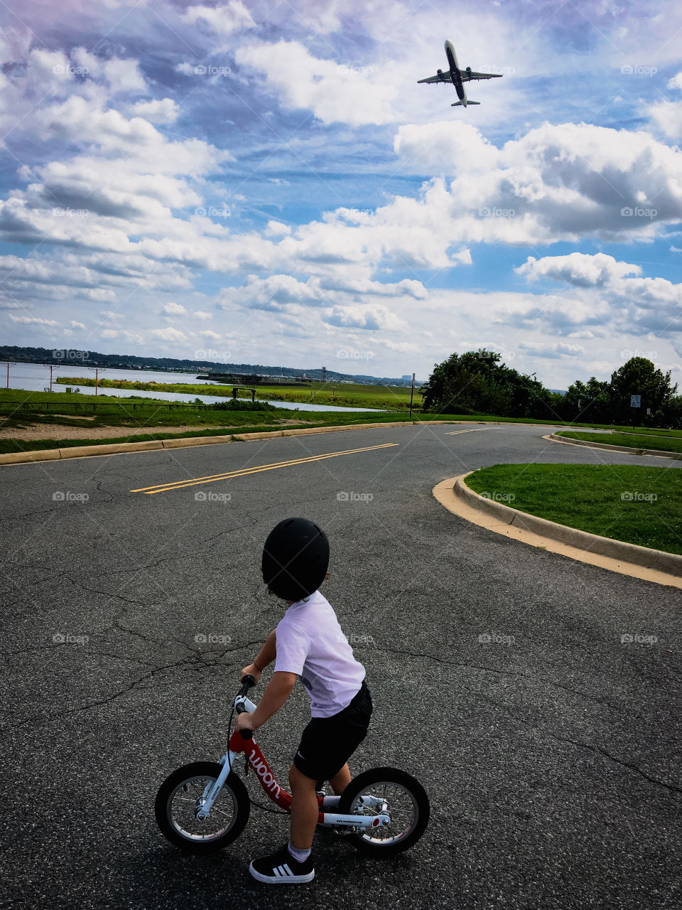 Kid riding a bike while watching an airplane take off 