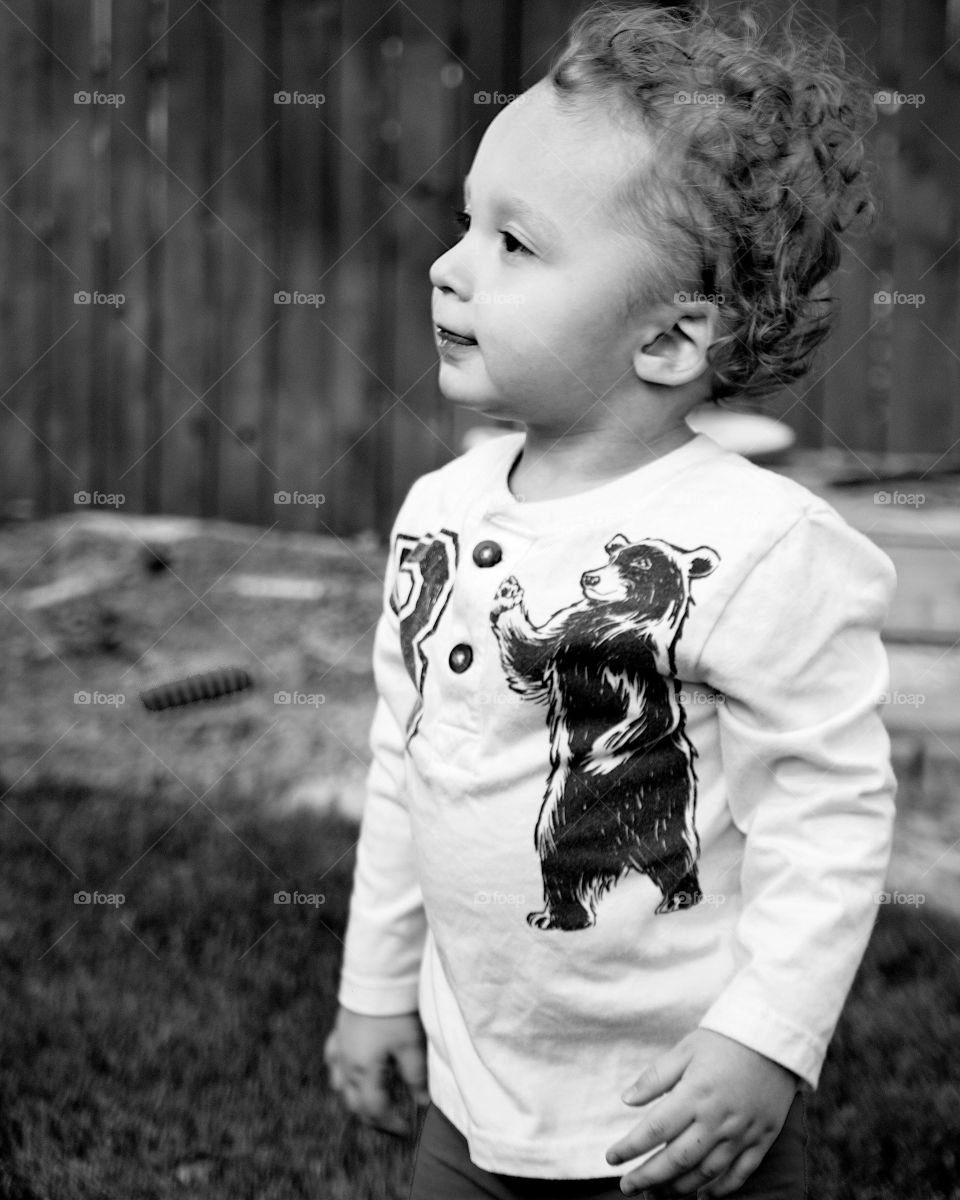 An adorable curly haired toddler boy being very attentive while playing in the backyard on a sunny summer day. 