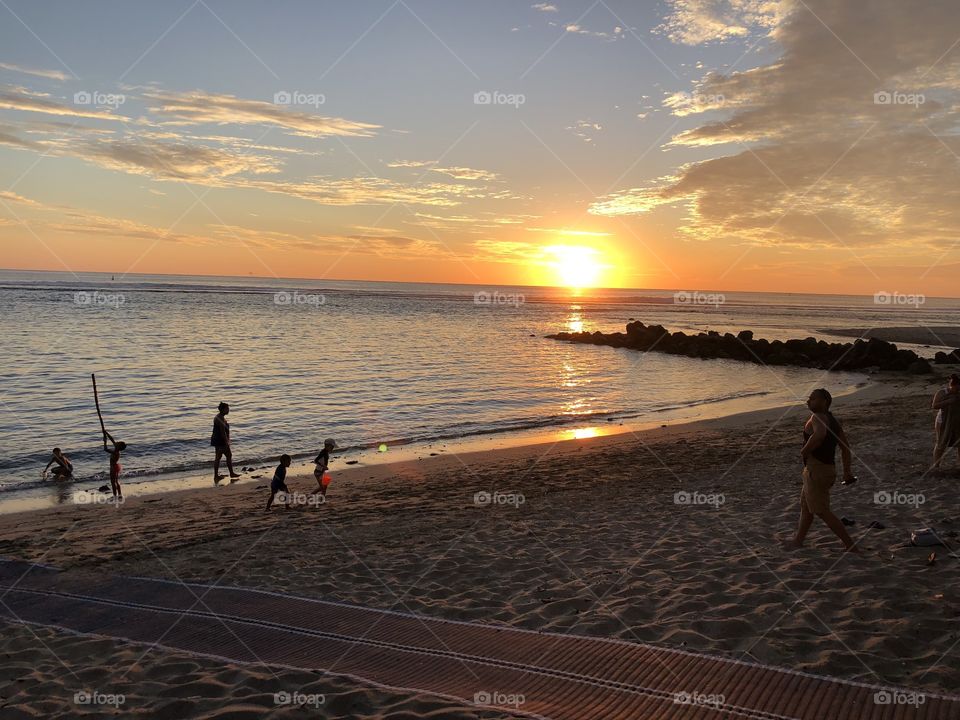 Family playing on the soft sand of the beach as the sun sets over the ocean. Image captured on Reunion Island, France 
