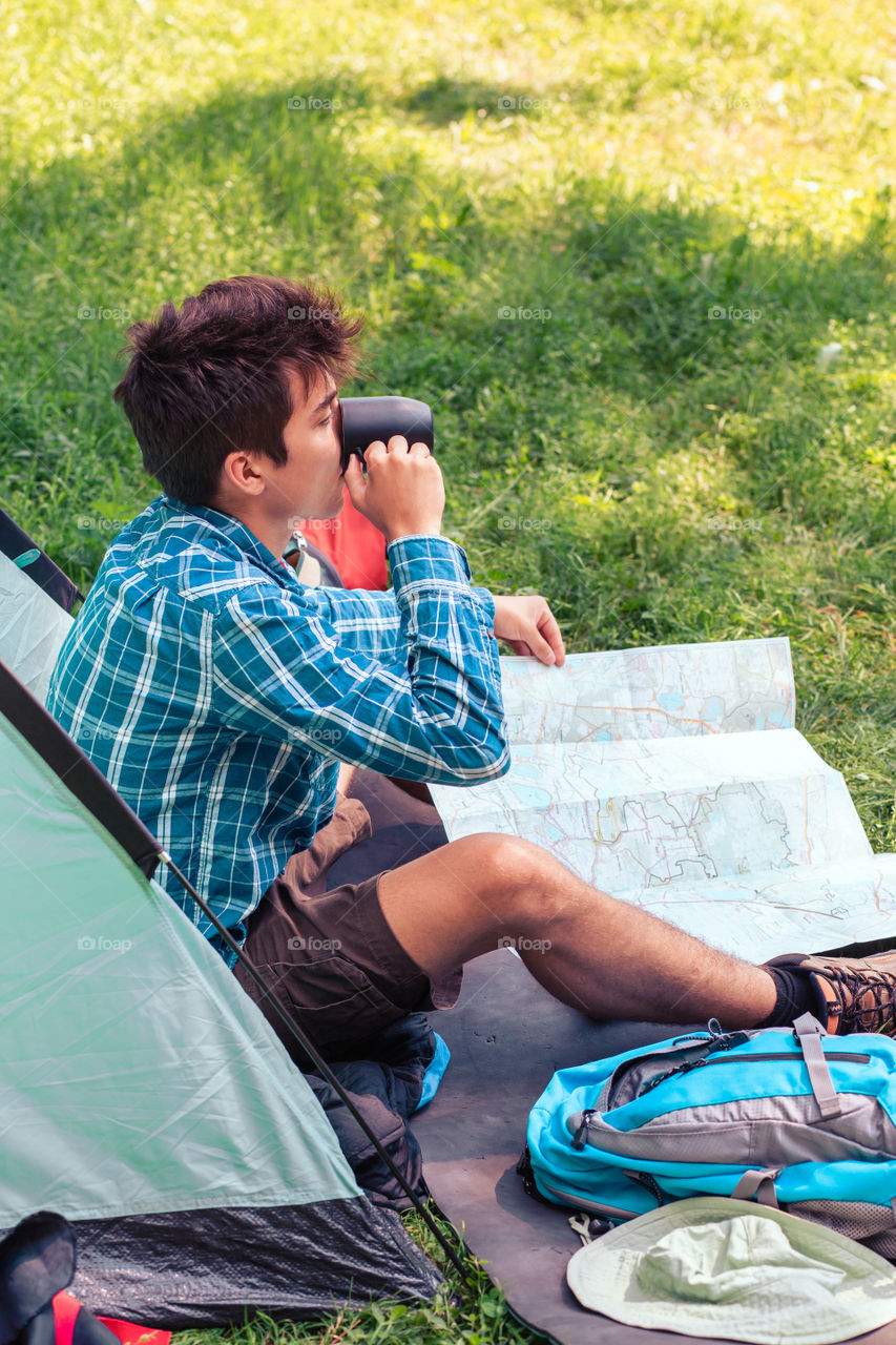 Spending a vacation on camping. Young man planning next trip and drinking a coffee