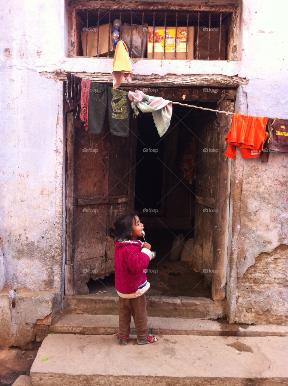 Little Indian girl standing in front of her house with spoon. In India