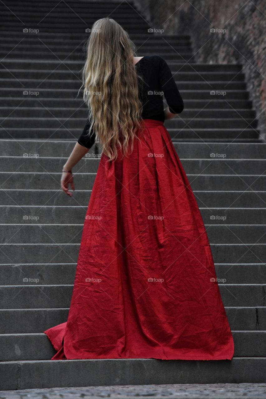 Blonde long hair woman in long red skirt standing on the stairs in old Prague