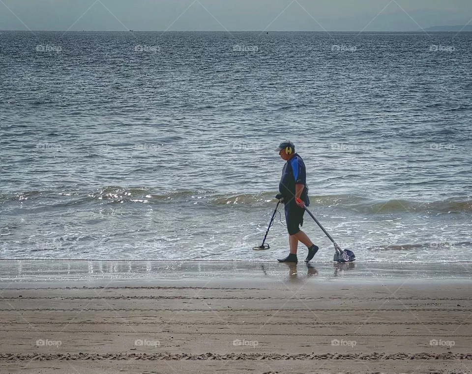 Man with a metal detector walking on a beach