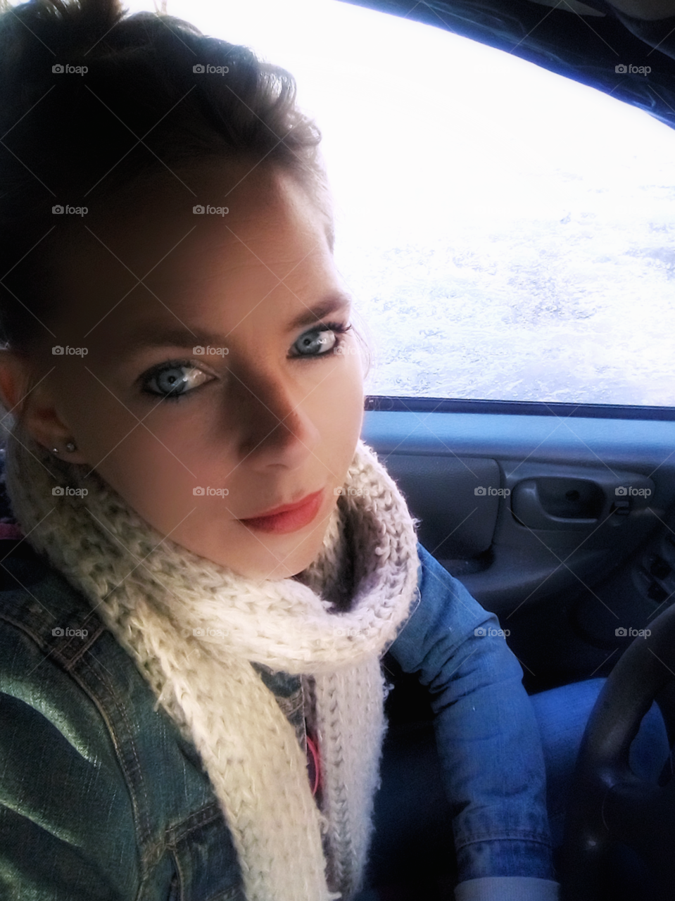 woman wearing scarf sitting in a car next to window showing snow outside