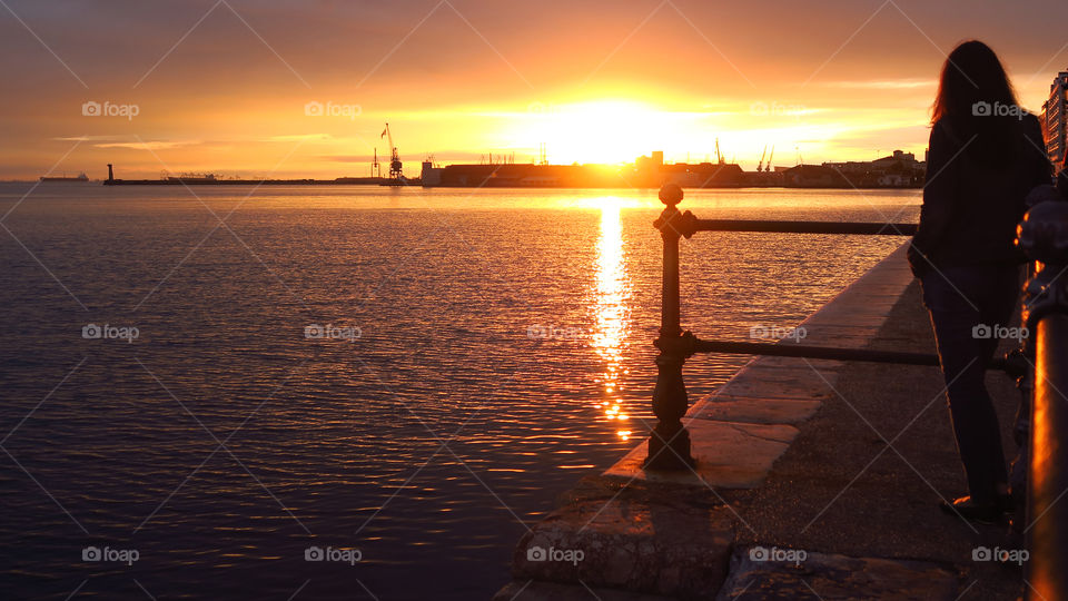 Thessaloniki -Greece. A girl is gazing at the sunset on the city's port. The old waterfront  is a major car-free pedestrian area.