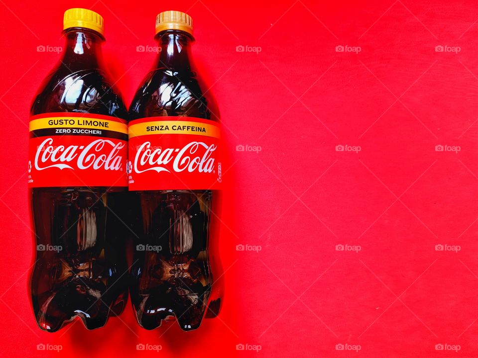 two bottles of Coca Cola resting on a red background