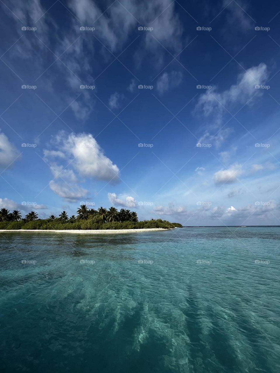 Every cloud has a silver lining: A mesmerising design - a crystal clear lagoon and a dark blue sky with scattered clouds and greenery of an island in the Maldives.