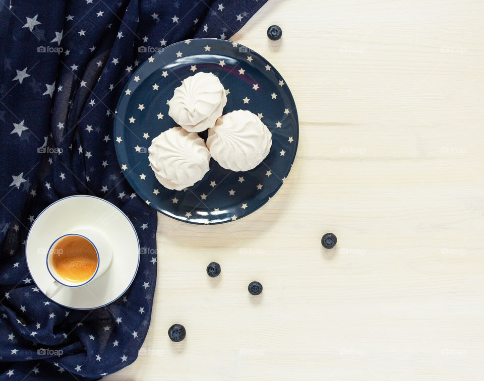White and blue contrast food photo. A pleasant morning with a Cup of coffee, marshmallows and blueberries on a white wooden table with a copy space decorated with blue textiles with stars evoking an American image and holiday