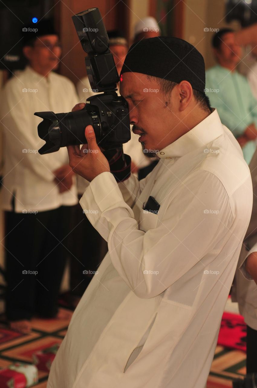 Portrait of an Asian man dressed in Muslim clothes aiming at a photo or video.