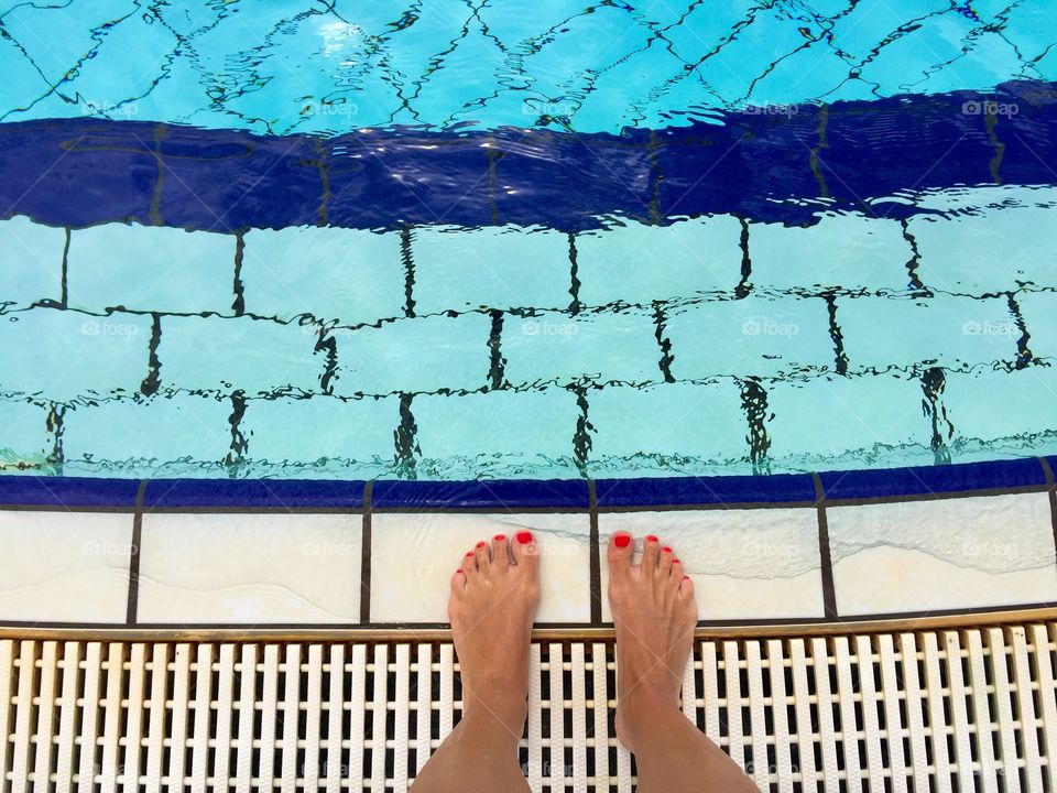 Woman's feet with red nails by the pool ready to get into the water