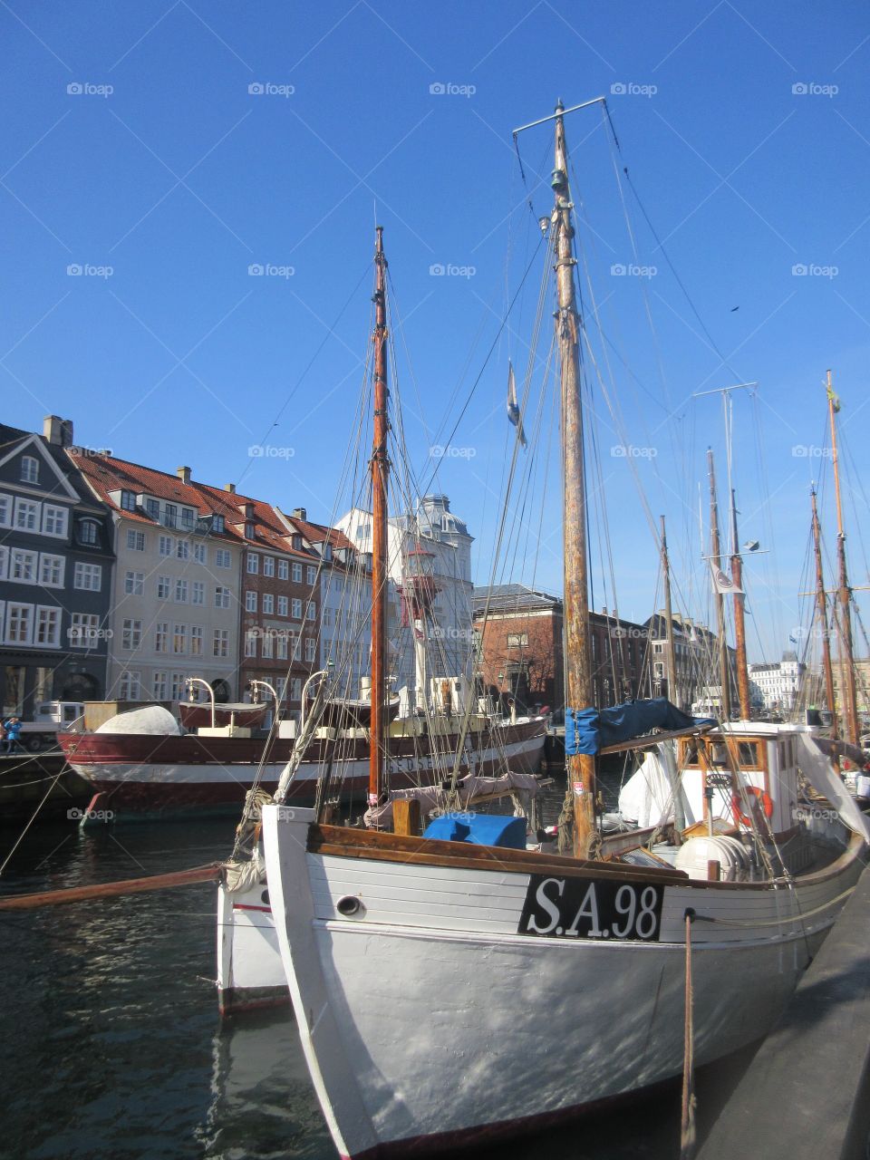 Boat in port in Denmark with clear, blue sky along with traditional buildings in the background. 